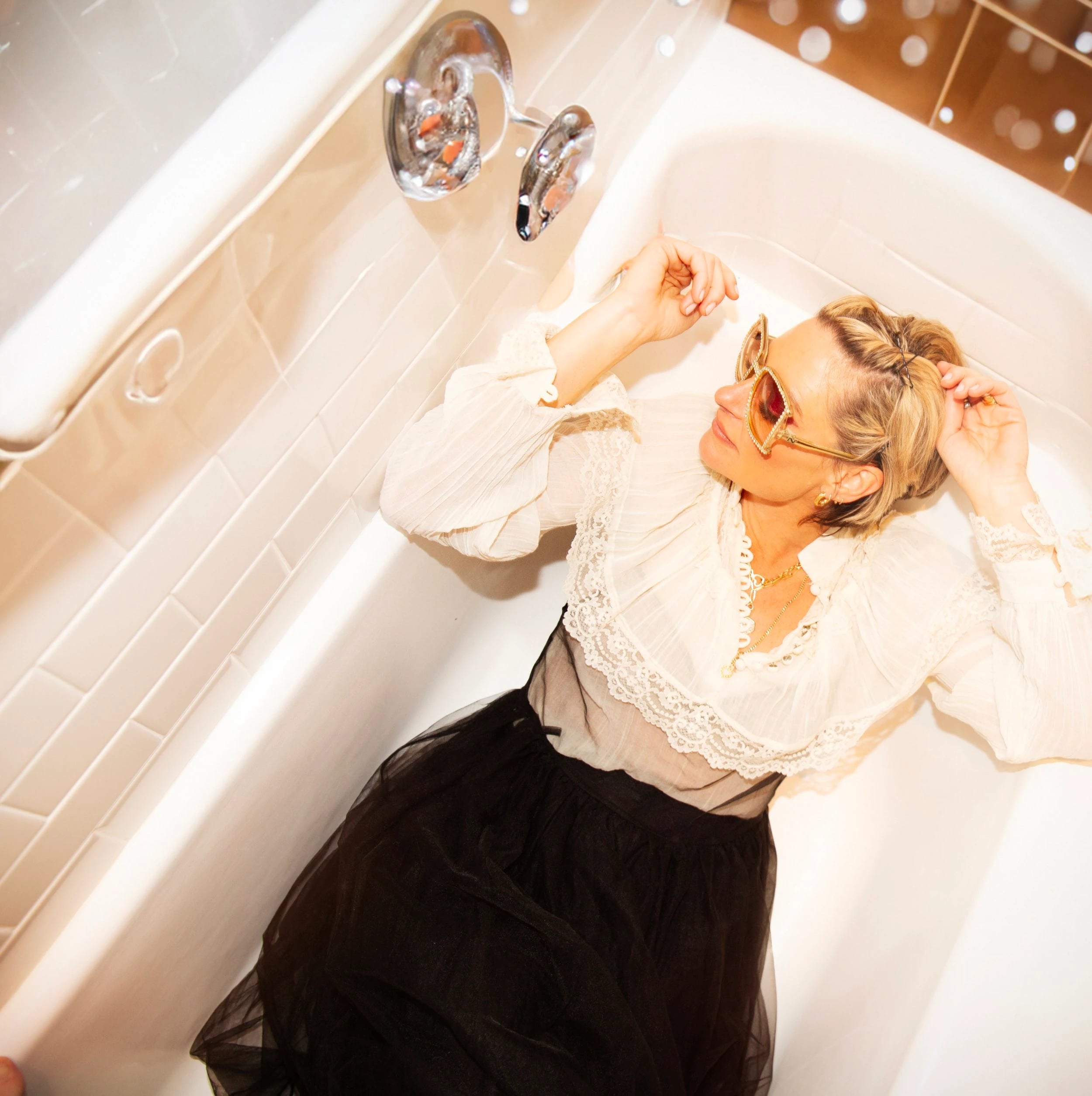 Sara Barnthouse relaxing in a bathtub, wearing sunglasses and a white blouse